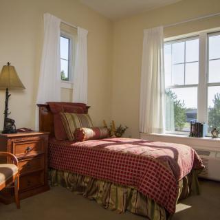 A cozy bedroom with a single bed and abundant natural light from large windows.