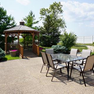 A serene outdoor patio area with a glass table and chairs, adjacent to a charming gazebo surrounded by greenery.