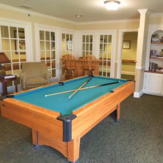 A game room featuring a pool table with cues and chairs in the background.