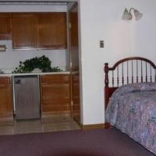 A cozy room featuring a bed and a small kitchenette with wooden cabinets.