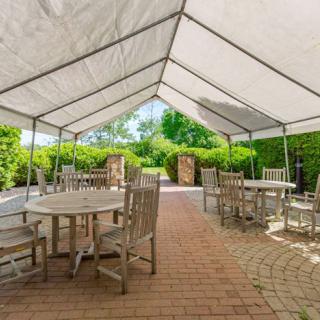 A spacious outdoor seating area under a white canopy with wooden tables and chairs on a brick patio.