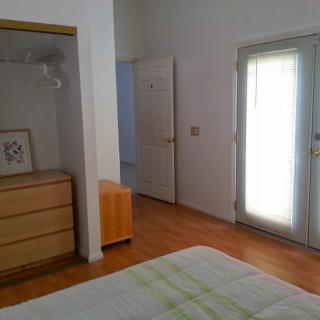 A minimalist bedroom interior featuring a dresser, open door, and window with natural light.