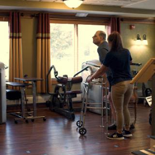 A physical therapist assisting an elderly person during a rehabilitation session in a therapy room.