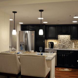A modern kitchen with black cabinets and pendant lighting, featuring an island with seating and stainless steel appliances.
