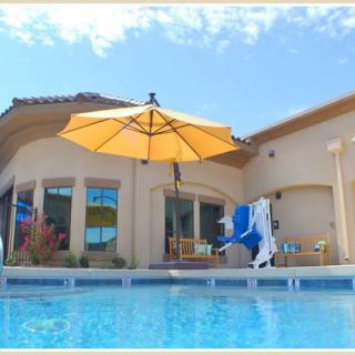 A luxurious house with a swimming pool and patio, featuring an umbrella and outdoor seating under a clear blue sky.
