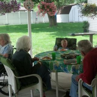 A group of elderly people sitting around a table on a patio, enjoying a meal together.