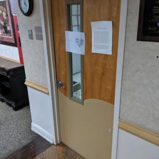 A wooden office door with a glass panel, featuring notices attached.