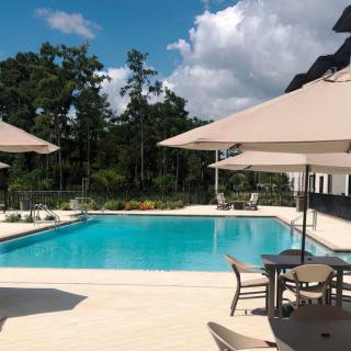 A tranquil outdoor swimming pool area with umbrellas and seating under a clear blue sky.