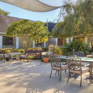 A spacious outdoor patio area featuring elegant metal furniture, surrounded by greenery and shaded by a fabric canopy.