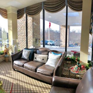 A cozy lounge area with a comfortable sofa, decorated with cushions and surrounded by large windows allowing natural light to fill the space.