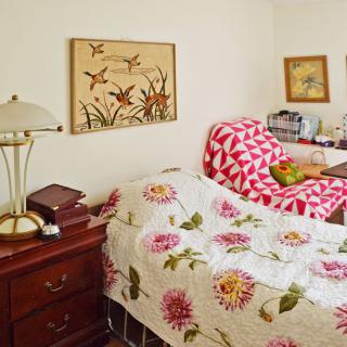 A cozy bedroom featuring a floral-patterned quilt, an armchair with a geometric design, and various decorative elements.
