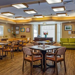A cozy dining area featuring wooden tables and chairs, with artwork adorning the walls and soft lighting creating a welcoming ambiance.