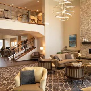 A spacious and elegantly designed modern living room featuring luxurious furniture, a stylish chandelier, and an open-plan layout with a staircase.