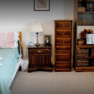 A cozy bedroom with a neatly arranged nightstand, dresser, and shelves.