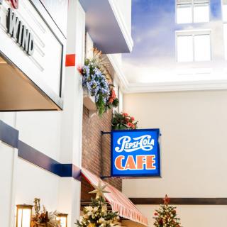 A vibrant cafe sign adorns the interior, surrounded by decorative flowers and soft lighting.