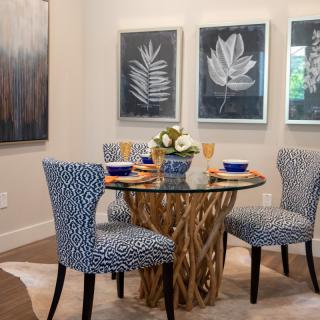 A modern dining room with a glass-top table and patterned chairs, complemented by botanical artwork on the walls.