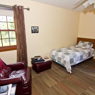 A cozy bedroom with a bed, leather chair, and a window providing natural light.