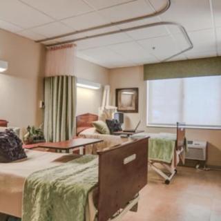 A hospital room with two patient beds, separated by curtains and a window with blinds.