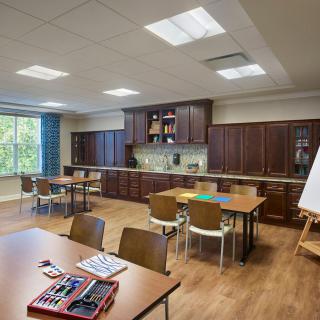 A multipurpose room featuring kitchen appliances, tables and chairs arranged for a classroom setting.