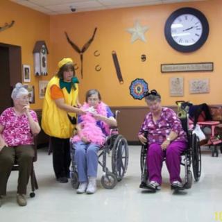 Elderly residents in a nursing home gather together, with one dressed in a playful costume.