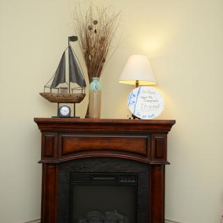 A cozy fireplace mantle decorated with a model sailboat, a lamp, a decorative plate, and a vase with dried branches.