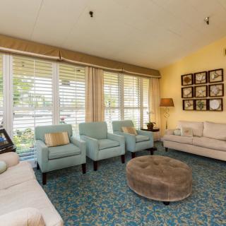 A cozy living room with comfortable seating, a patterned carpet, and large windows with blinds.