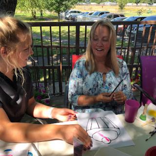 Two women enjoying a creative moment outdoors, working on art together.