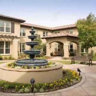 A beautiful courtyard featuring a central fountain surrounded by well-maintained gardens and a large building in the background.