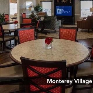 A cozy dining area with red cushioned chairs and a round table, set in a community space labeled 'Monterey Village'.