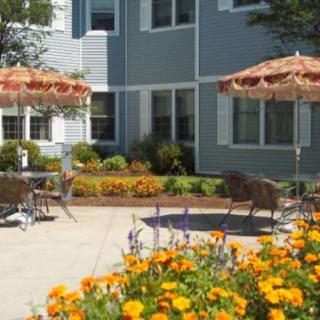 A sunny outdoor patio with colorful flowers and seating under umbrellas next to a residential building.