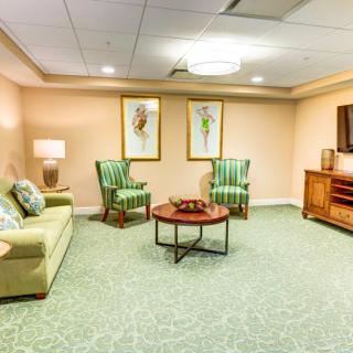 A cozy living room with a sofa, two chairs, a coffee table, and a television, featuring soft lighting and wall art.