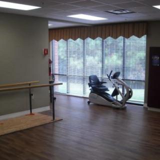A well-lit exercise room featuring a stationary bike and handrails, with large windows allowing natural light.
