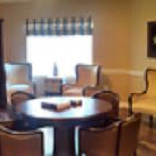 A cozy living room with a round table surrounded by chairs and a window with curtains.
