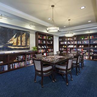 A well-organized library with a large table and chairs, surrounded by bookshelves under elegant chandeliers.