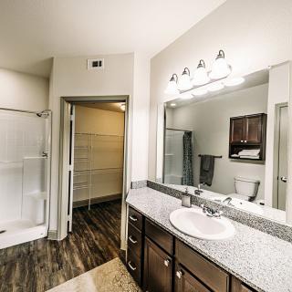 A modern bathroom with a granite-topped vanity, large mirror, and glass shower enclosure.