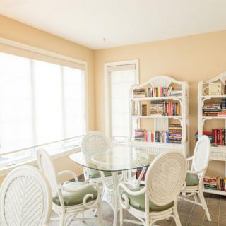 A cozy dining room with a glass table, cushioned chairs, and bookshelves filled with books.