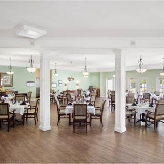 A spacious and elegantly decorated dining area with neatly arranged tables and chairs, featuring chandeliers and a wooden floor.