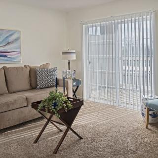 A cozy living room with a sofa, coffee table, and window blinds letting in natural light.