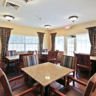 A cozy dining area with multiple tables and chairs, surrounded by large windows and curtains.
