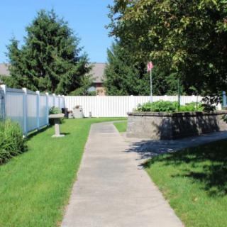 A quiet backyard with a sidewalk leading to a garden area, bordered by a white fence.