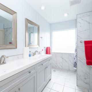 A modern bathroom with white tiles, featuring a sink, mirror, and red towels.