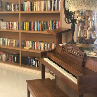 A cozy corner featuring a wooden piano and a bookshelf filled with various books.