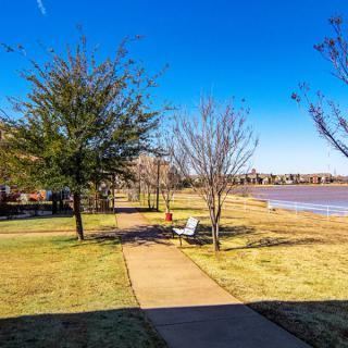 A scenic view of a park with a pathway leading to benches by the lake under a clear blue sky.