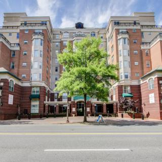 A multi-story residential building with a tree in front, located on a city street.