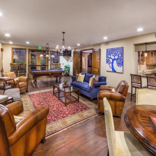 A cozy living room with elegant leather chairs, a blue sofa, and a vibrant rug, highlighted by warm lighting and tasteful artwork.