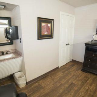 A room with a sink, mirror, dresser, and wall art.