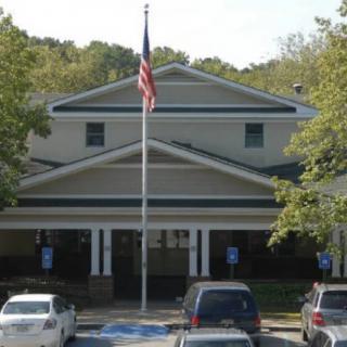 A building with an American flag in front, surrounded by trees and parked vehicles.