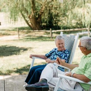 An elderly couple enjoying a conversation while seated in chairs outdoors.