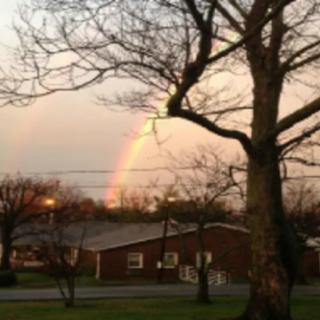 A rainbow arcs over a suburban house, framed by trees.