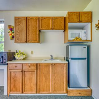 A compact kitchen with wood cabinetry, featuring a microwave, refrigerator, and sink.